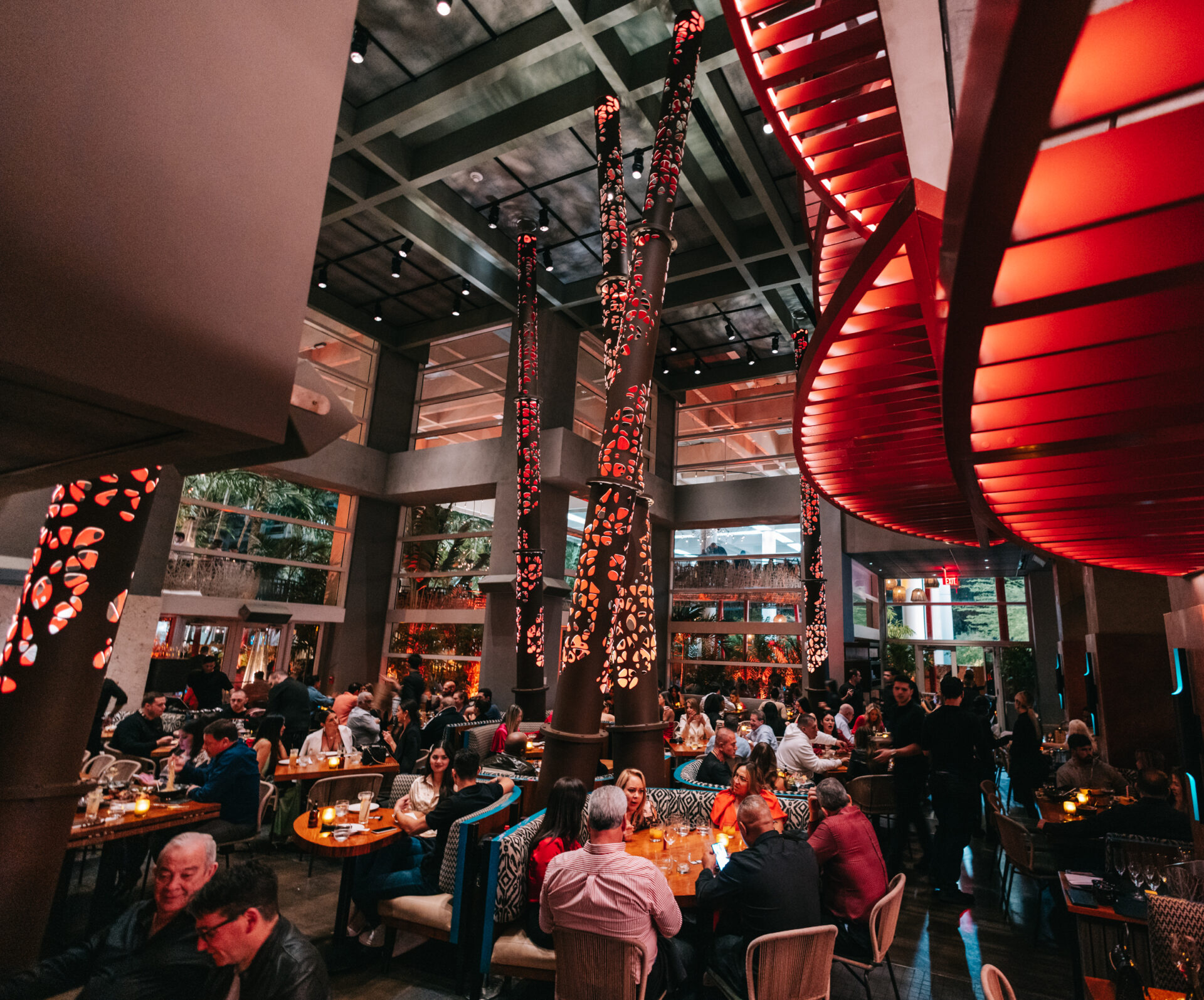 Un ristorante vivace con soffitti alti, grandi finestre, arredamento moderno e suggestive luci a spirale rosse. I clienti sono seduti ai tavoli e si godono i pasti e le conversazioni sotto una calda illuminazione ambientale.