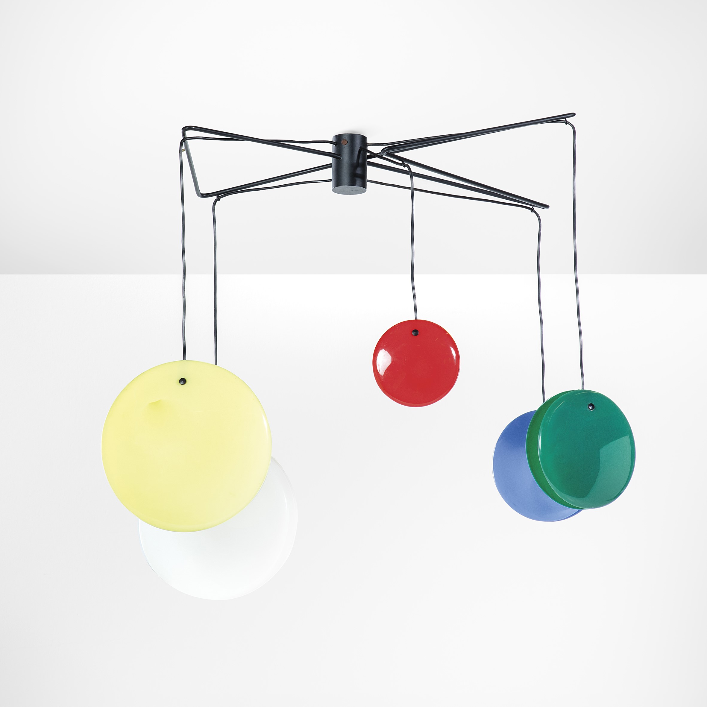 Una moderna lampada da soffitto con un design astratto con aste metalliche nere e cinque dischi circolari colorati appesi in giallo, rosso, verde, blu e bianco. La lampada è posta su uno sfondo bianco semplice.