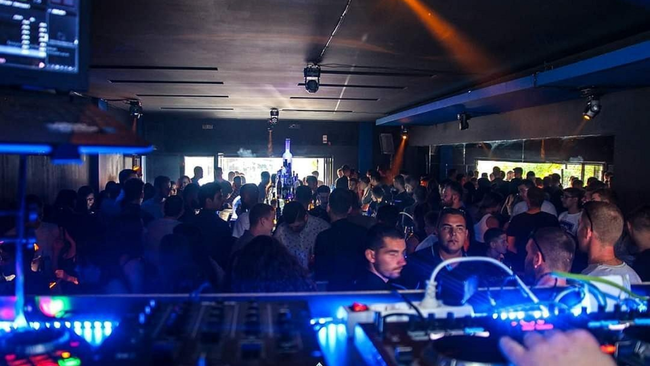 Una scena di discoteca affollata con una cabina del DJ in primo piano evoca l'energia dell'après-ski di Cervinia. Le persone ballano e socializzano sotto una luce soffusa, mentre luci colorate esaltano l'atmosfera vibrante.