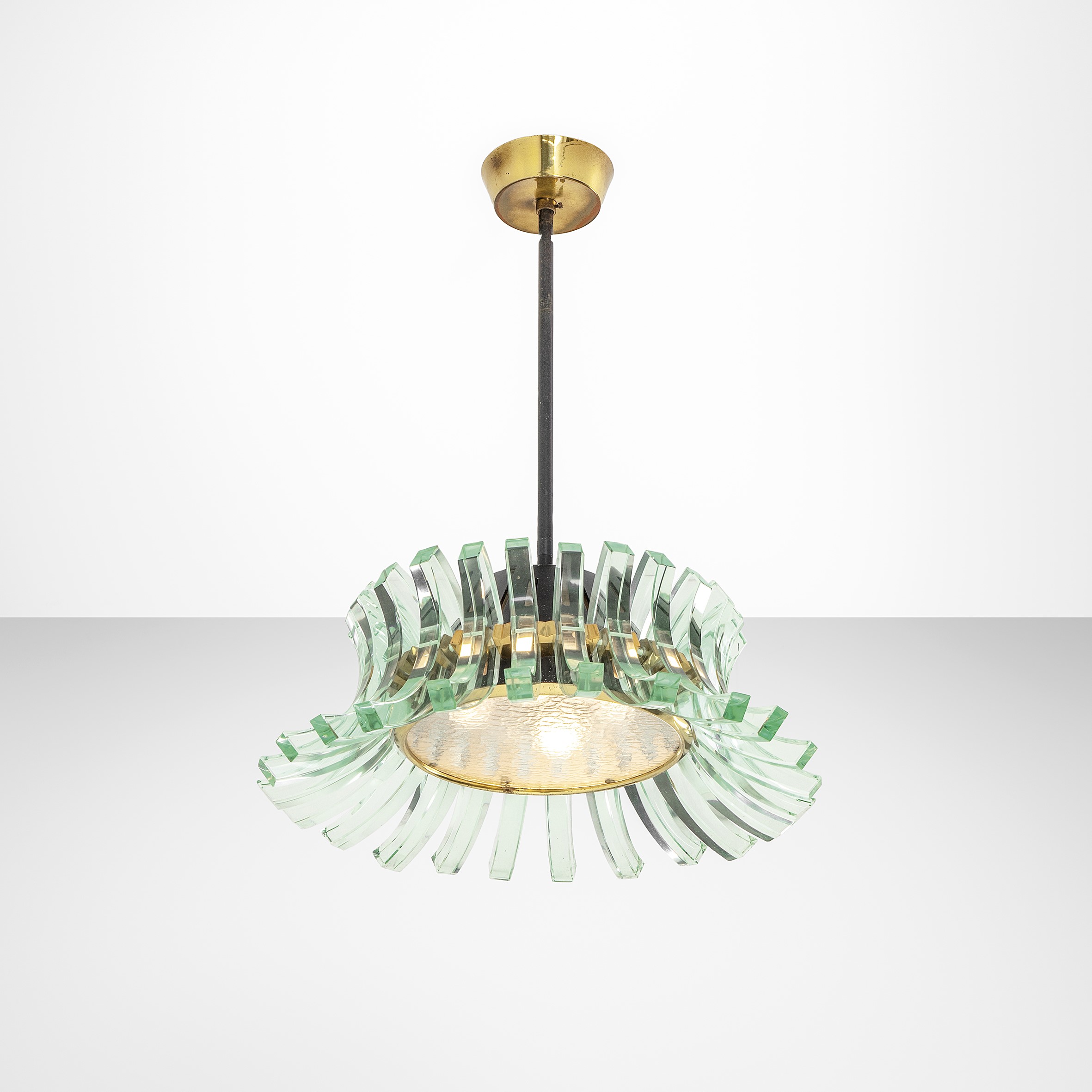 Un lampadario moderno con un attacco a soffitto dorato. Presenta un design circolare in vetro che ricorda petali sovrapposti, con una singola lampadina al centro. Gli elementi in vetro trasparente riflettono la luce, creando un aspetto elegante e artistico.