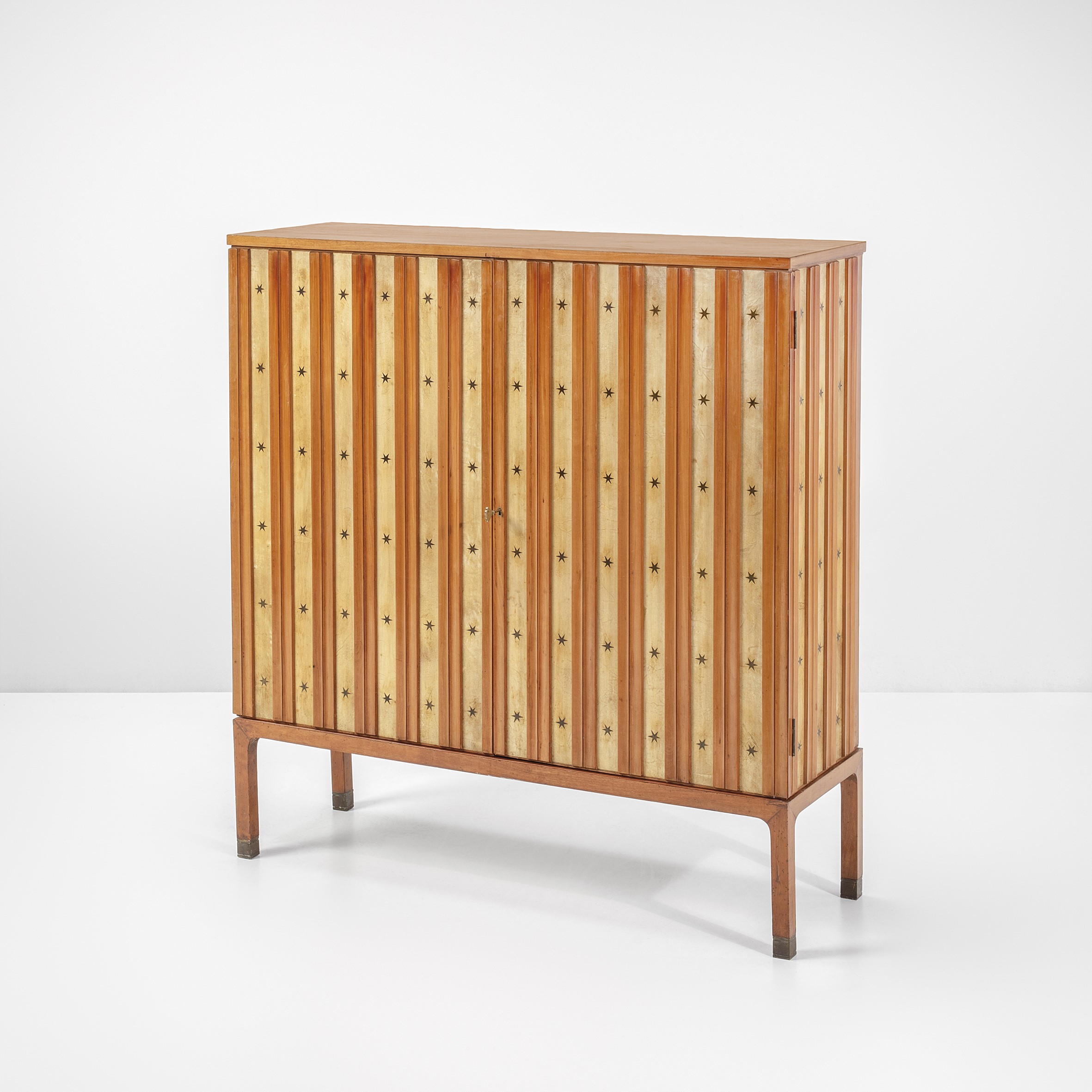 Un mobiletto vintage in legno con pannelli a strisce verticali che presentano piccoli motivi a stella. Si regge su quattro gambe e ha un design semplice ed elegante su uno sfondo bianco semplice.