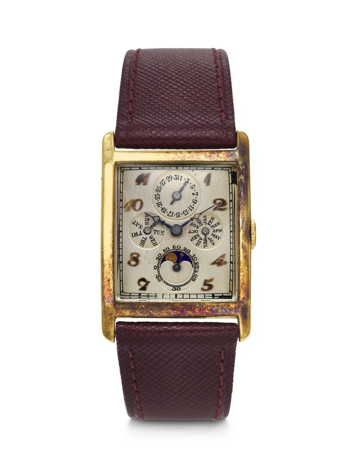 Un orologio da polso rettangolare in oro d'epoca, un tempo esposto in un'asta di orologi di Christie's, con lunetta usurata, quadrante crema con più quadranti secondari, numeri dorati e cinturino in pelle testurizzata bordeaux con cuciture abbinate.