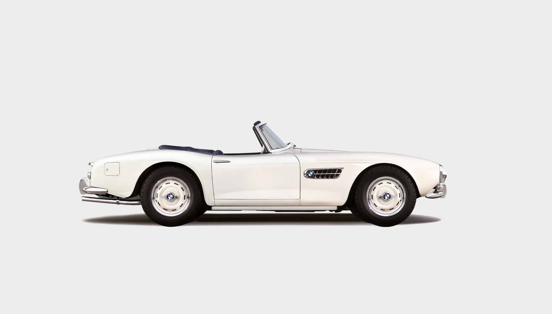 Una classica auto sportiva decappottabile bianca con la capote abbassata, vista di lato su uno sfondo chiaro, che ricorda l'eleganza senza tempo del Concorso d'Eleganza Villa d'Este.