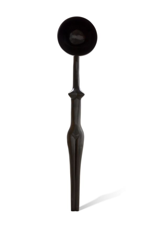 Un cucchiaio nero allungato e scultoreo con una ciotola rotonda, un collo stretto e un manico affusolato e astratto che ricorda una figura umana stilizzata, esposta su uno sfondo bianco.