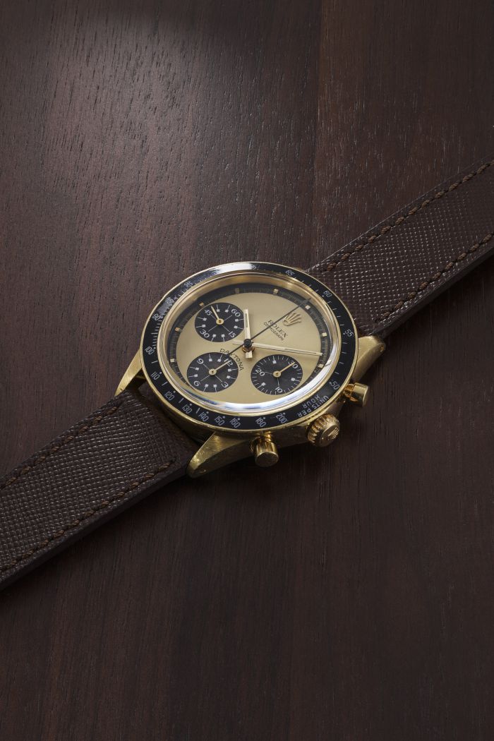 Un orologio da polso vintage con cassa in oro, lunetta nera e tre quadranti secondari è montato su un cinturino in pelle marrone testurizzata, esposto su una superficie di legno scuro: un pezzo ideale per gli appassionati di orologi lusso nuove tendenze.