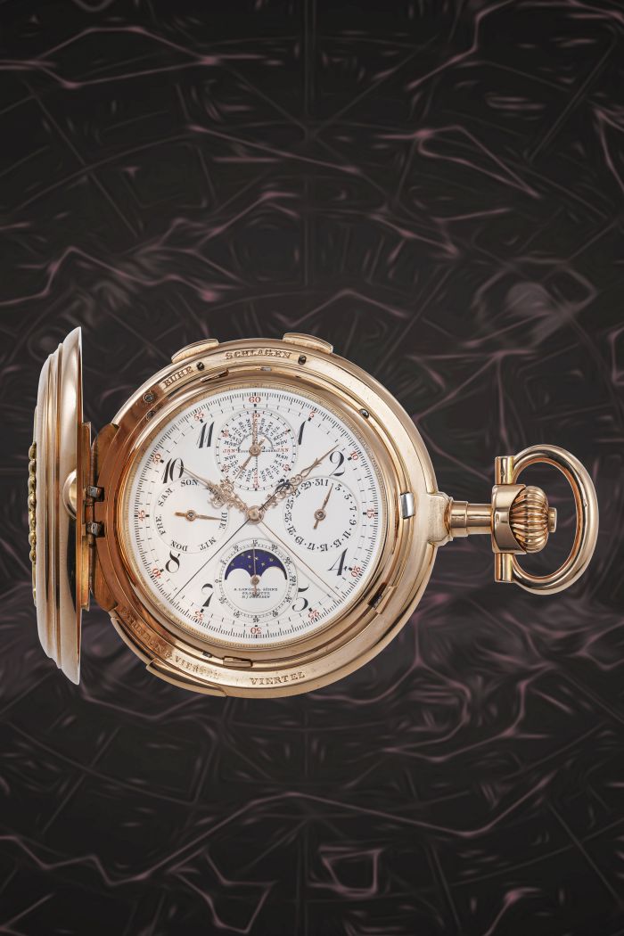 Un orologio da tasca in oro con coperchio aperto presenta quadranti multipli e lancette intricate, tra cui un indicatore delle fasi lunari: uno squisito esempio di orologi lusso nuove tendenze su uno sfondo di motivi vorticosi scuri e astratti.