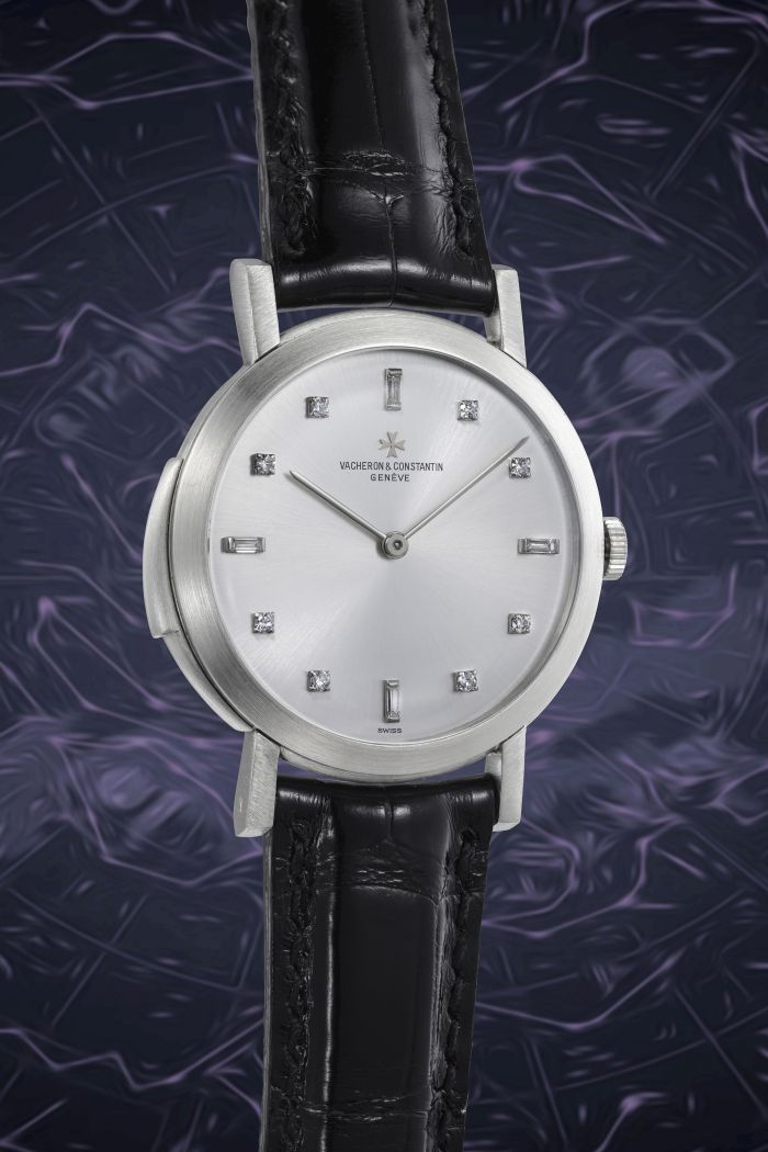 Un orologio da polso Vacheron Constantin in argento con cinturino in pelle nera, indici delle ore in diamanti e un design minimalista esemplificano le nuove tendenze orologi lusso, esposte su uno sfondo viola scuro e astratto.