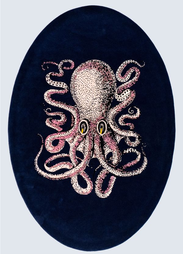 Un tappeto ovale con sfondo blu scuro presenta un'illustrazione stilizzata di un polipo rosa chiaro con tentacoli arricciati e due occhi, che ricorda l'audace stile artistico di Stefano Gabbana.
