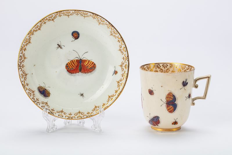 Set di tazze e piattini in porcellana della collezione Asta di Stefano Gabbana, decorati con farfalle rosse e arancioni, piccoli insetti e bordi con dettagli dorati, elegantemente esposti su uno sfondo bianco.