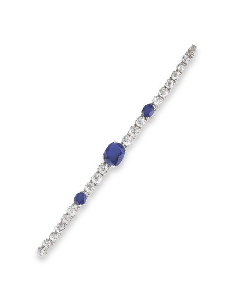 Un bracciale sottile ed elegante incastonato con diamanti bianchi rotondi e tre prominenti zaffiri blu ovali, che ricordano il fascino lussuoso di un orologio Bulgari Serpente, esposti su uno sfondo bianco.