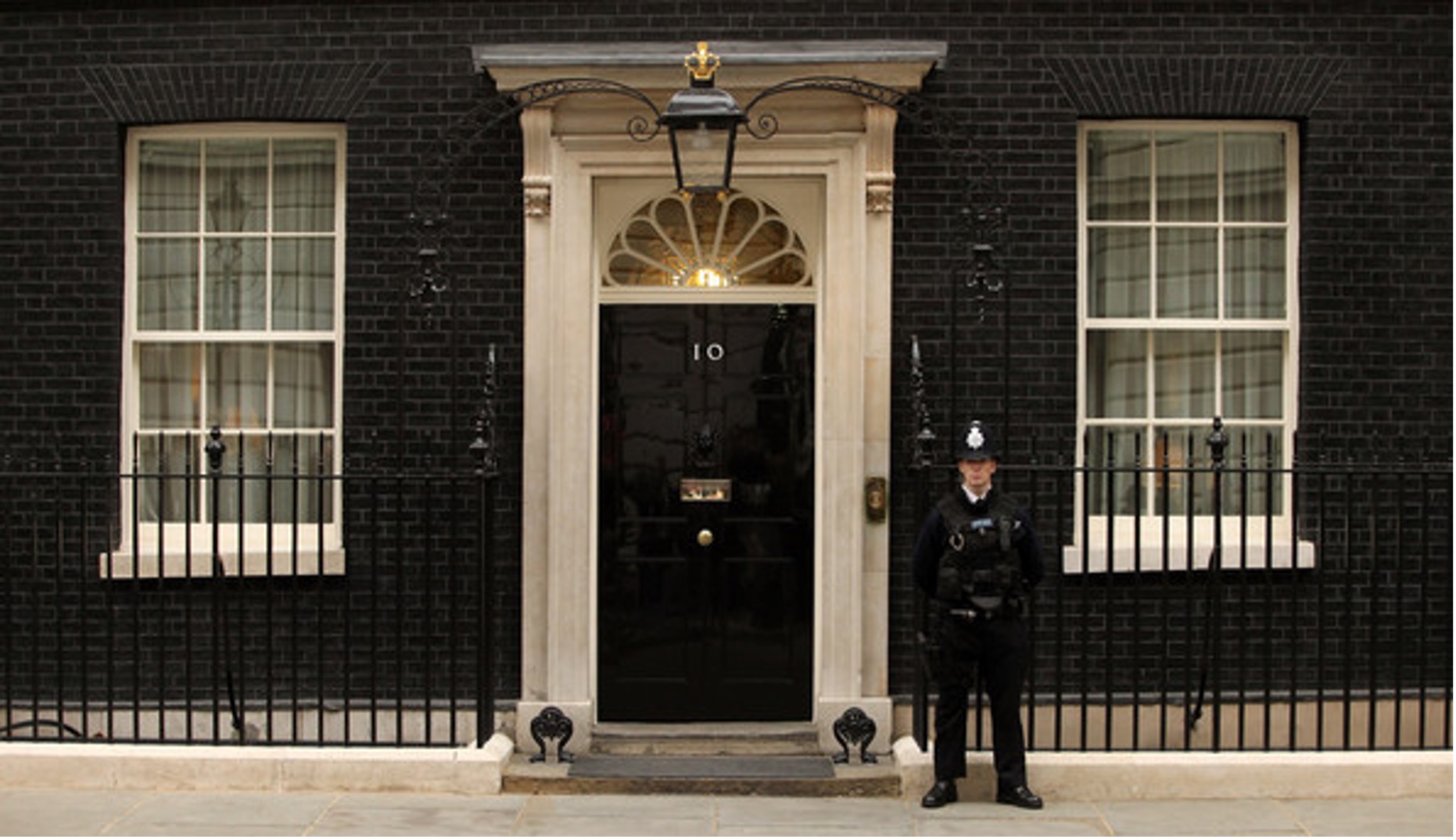 Un agente di polizia è di guardia davanti alla famosa porta nera del numero 10 di Downing Street, a Londra, la residenza ufficiale del Primo Ministro britannico, con due finestre e ringhiere nere che ricordano un quadro di Canaletto Asta.