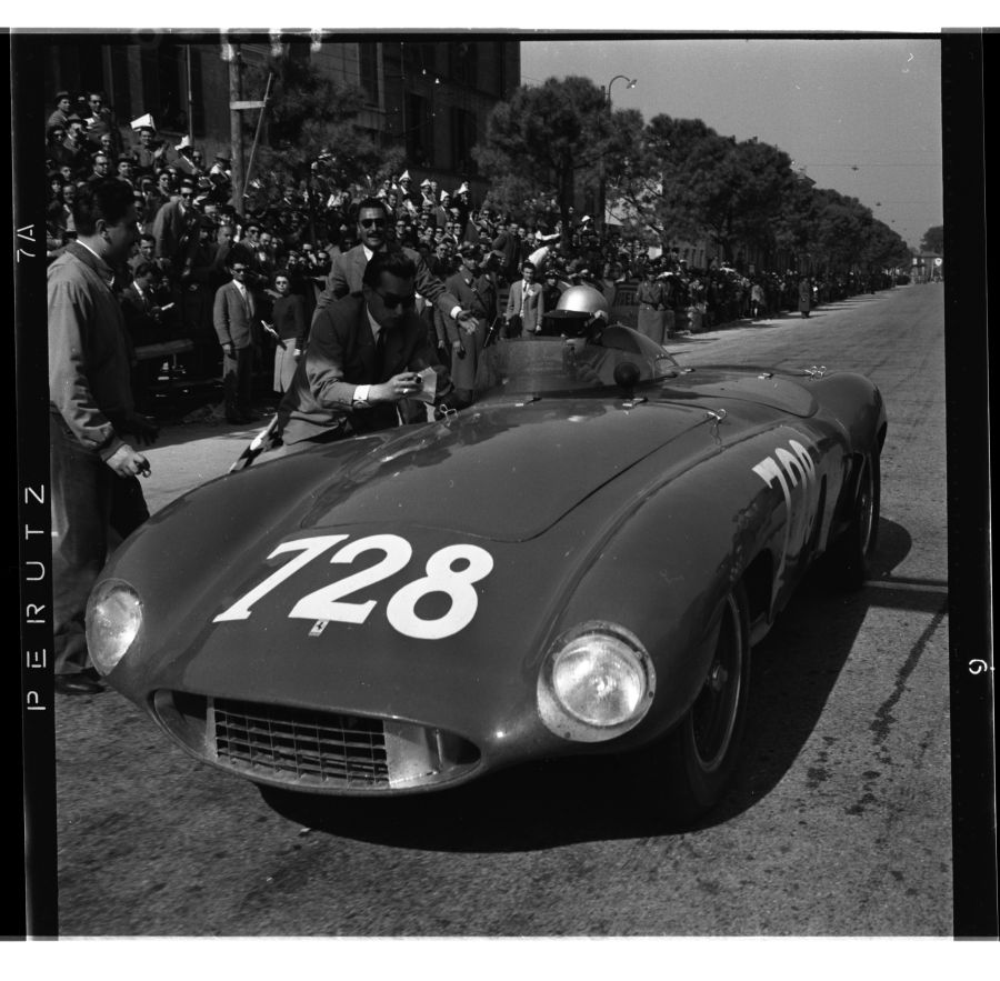 Un'auto da corsa d'epoca con il numero 728 sul cofano è parcheggiata su una strada durante la Mille Miglia 2025; un uomo si sporge, forse parlando con il pilota, mentre una folla di spettatori osserva sullo sfondo.