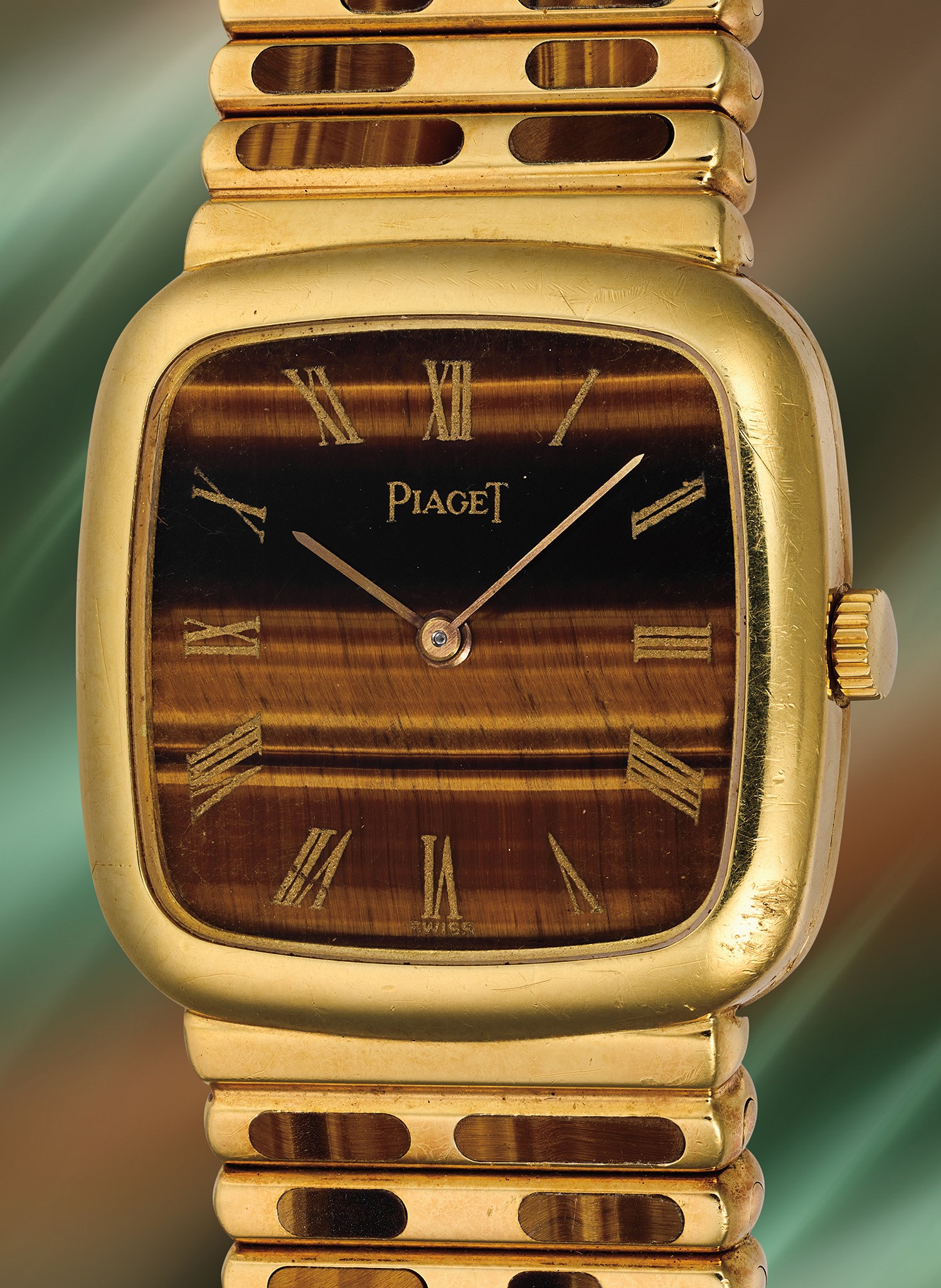 Un orologio da polso Piaget in oro con quadrante in occhio di tigre marrone, indici delle ore con numeri romani in oro e lancette delle ore e dei minuti in oro, su uno sfondo verde e marrone sfumato, che richiama l'eleganza dei modelli Phillips o Patek Philippe.