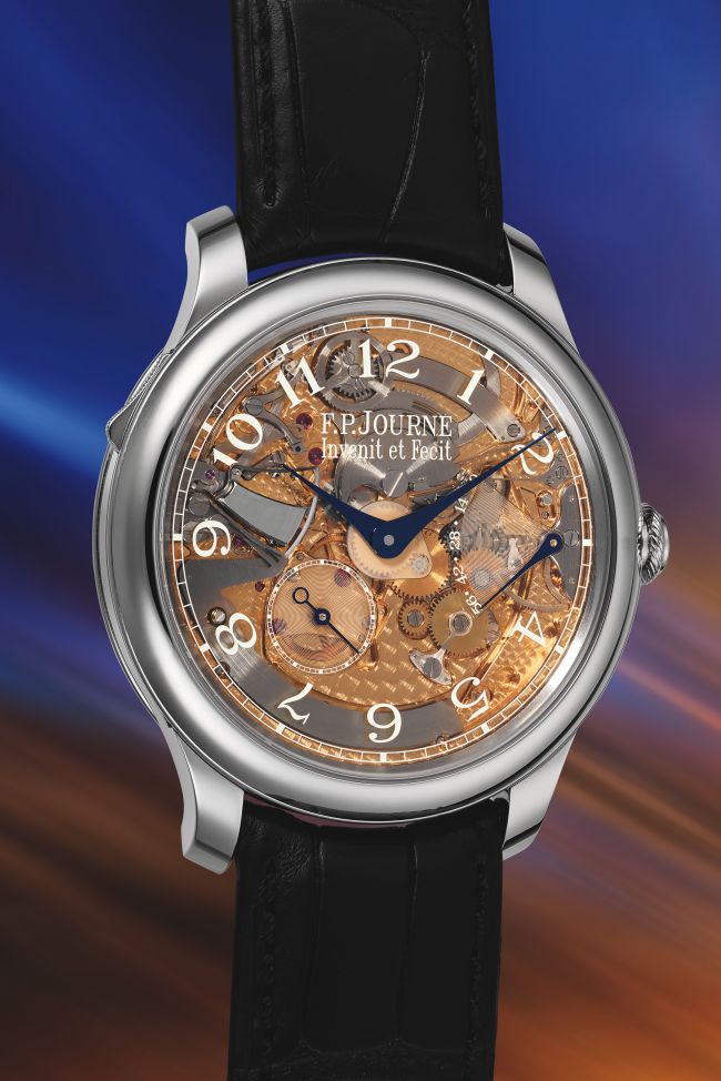 Un lussuoso orologio da polso F.P. Journe con quadrante scheletrato rivela ingranaggi intricati, lancette blu e numeri bianchi, che ricordano gli orologi visti da Phillips insieme a Patek Philippe, su uno sfondo sfocato e colorato di blu e arancione con un cinturino in pelle nera.