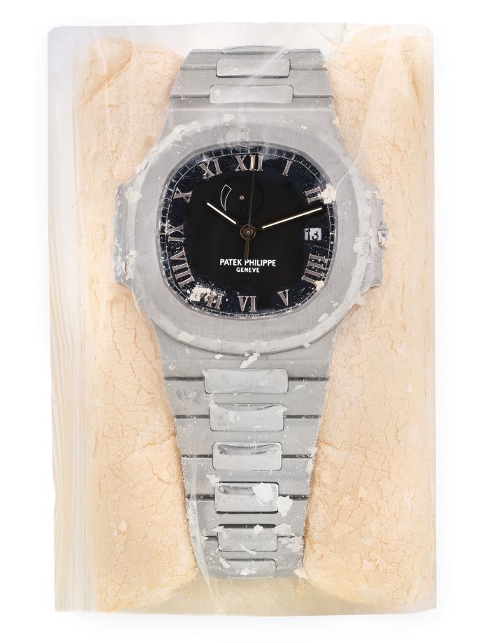 Un orologio da polso Patek Philippe d'argento, che ricorda i rari pezzi rolex visti all'asta, è sigillato all'interno di un sacchetto di plastica trasparente e circondato da polvere o briciole di colore chiaro, creando un'esposizione insolita e artistica.
