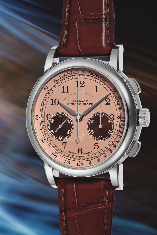 Un orologio da polso di lusso con quadrante rosa, cinturino in pelle marrone, cassa argentata e due quadranti secondari marrone scuro, con la scritta "A. Lange & Söhne" e "Flyback Chronograph", evoca l'aura prestigiosa di un Patek Philippe tra sfumature blu e arancioni sfumate.
