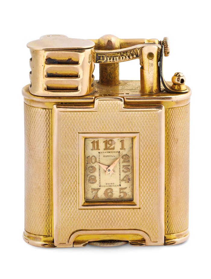 Un accendino Dunhill vintage in oro presenta un orologio quadrato integrato sulla parte anteriore, che ricorda il design di Rolex e Patek, con lati strutturati e componenti metallici dettagliati sulla parte superiore.