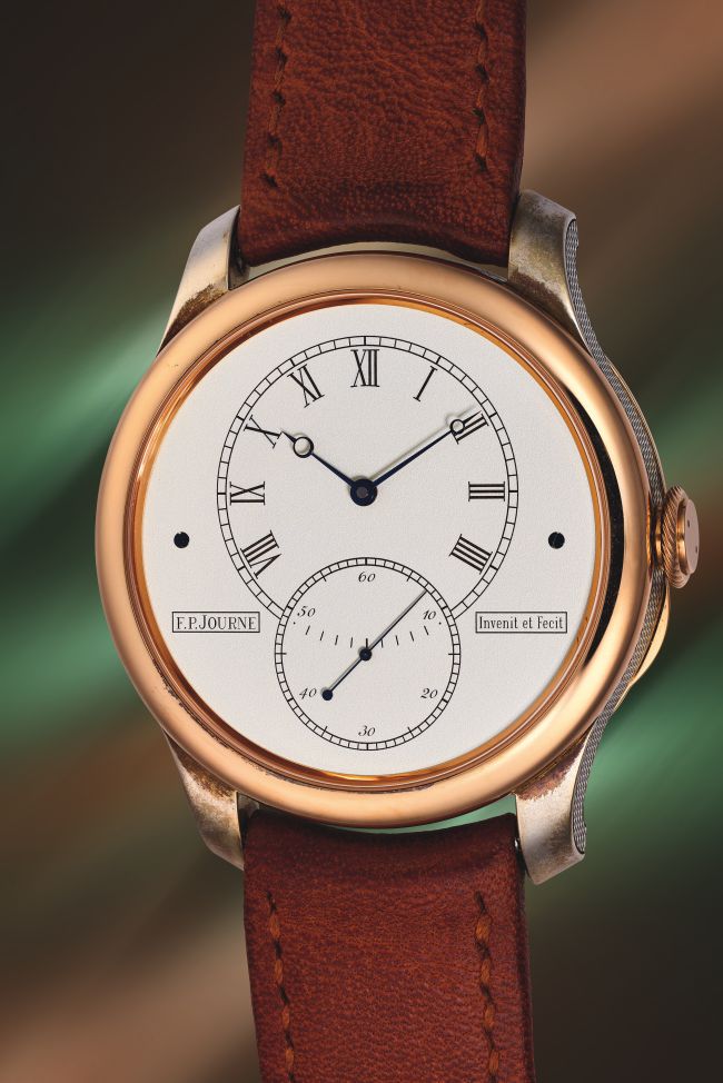 Un orologio da polso di lusso con cassa in oro, quadrante bianco, numeri romani neri e due quadranti secondari. Richiamando l'eleganza di Patek Philippe, presenta lancette in acciaio azzurrato, cinturino in pelle marrone e il nome F.P. Journe sul quadrante: un vero gioiello d'asta Phillips.
