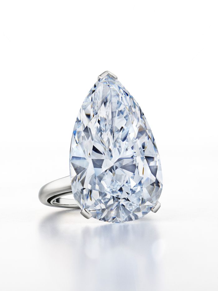 Un grande diamante trasparente a forma di pera incastonato in un semplice anello d'argento, esposto verticalmente su uno sfondo bianco.
