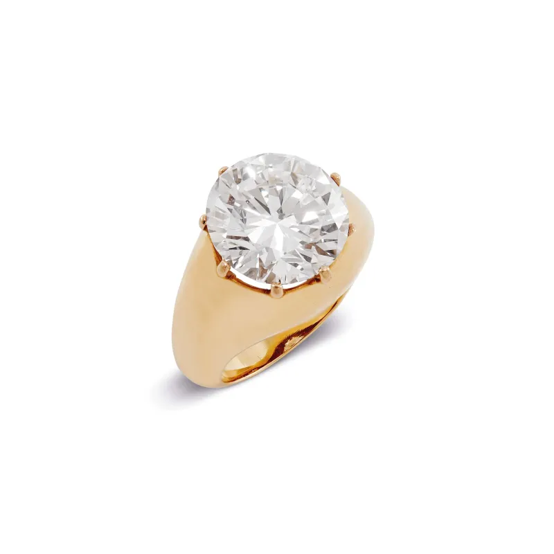 Un anello in oro con fascia larga, con al centro un grande diamante tondo e trasparente incastonato a griffe, che sprigiona l'eleganza senza tempo di un anello Patek Philippe Nautilus, esposto su uno sfondo bianco.
