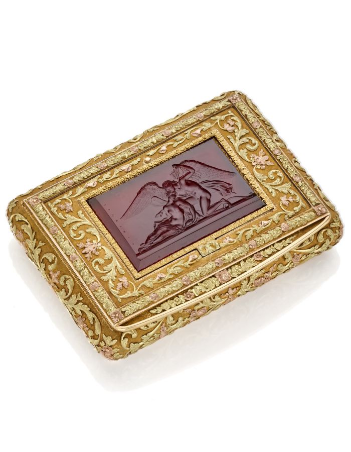 Scatola rettangolare decorata in oro con intricati motivi floreali, che ricordano l'arte di Lalique Asta, e un pannello rosso centrale con un rilievo dettagliato di due figure angeliche abbracciate.