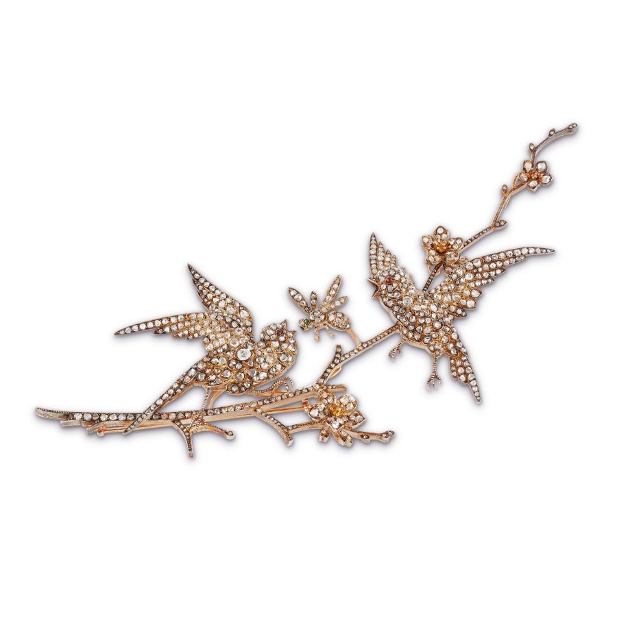 Una spilla decorativa in oro impreziosita da piccole gemme scintillanti, raffigurante due uccelli appollaiati su un ramo con delicati fiori, aggiunge un tocco di eleganza ispirata all'asta Patek Philippe Nautilus a qualsiasi outfit.