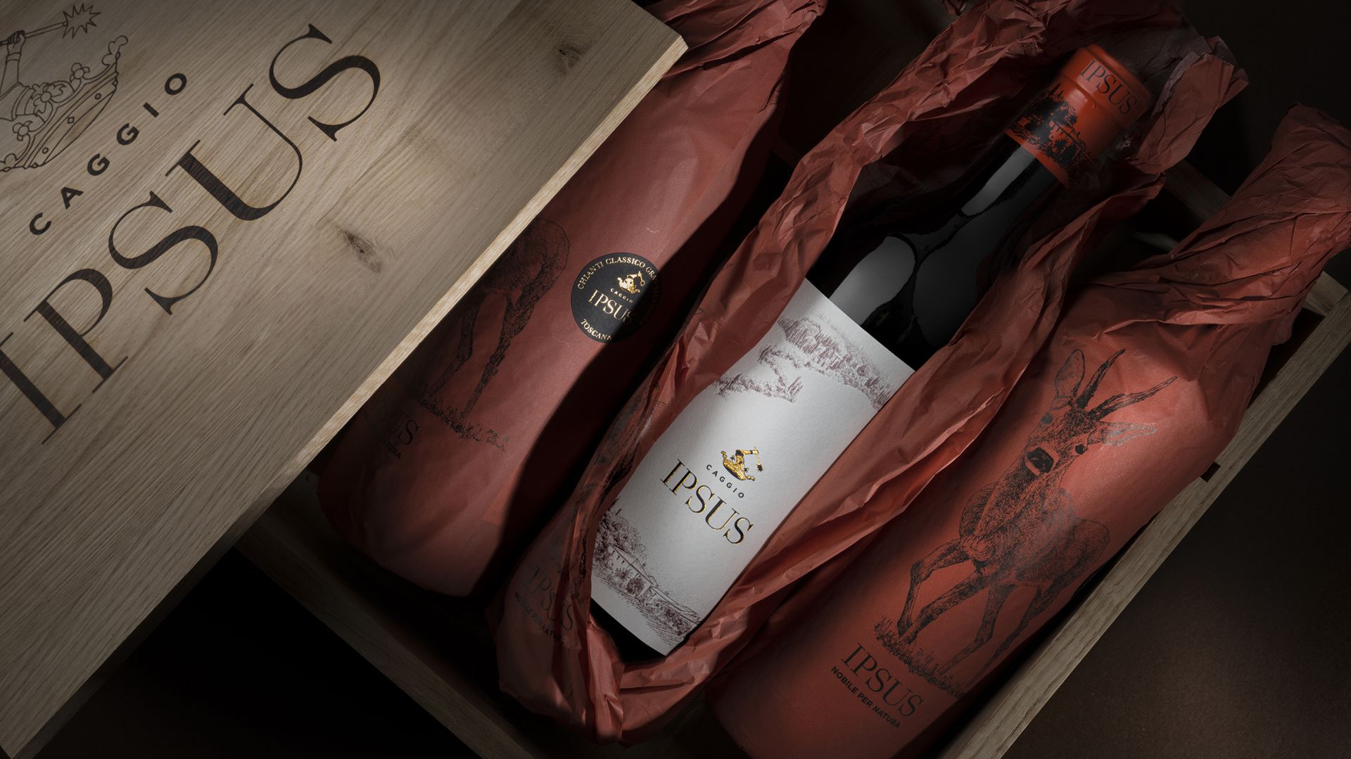 Una scatola di legno con l'etichetta "IPSUS" contiene quattro bottiglie di vino, tre avvolte in carta rossa con illustrazioni di animali e una non avvolta che mostra l'etichetta IPSUS, uno stemma e un design elegante.