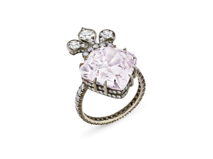 Un anello in argento decorato con una grande pietra preziosa diamante rosa Maria Antonietta al centro, impreziosita da pietre trasparenti più piccole e da un intricato design a forma di fiocco sopra la gemma principale.