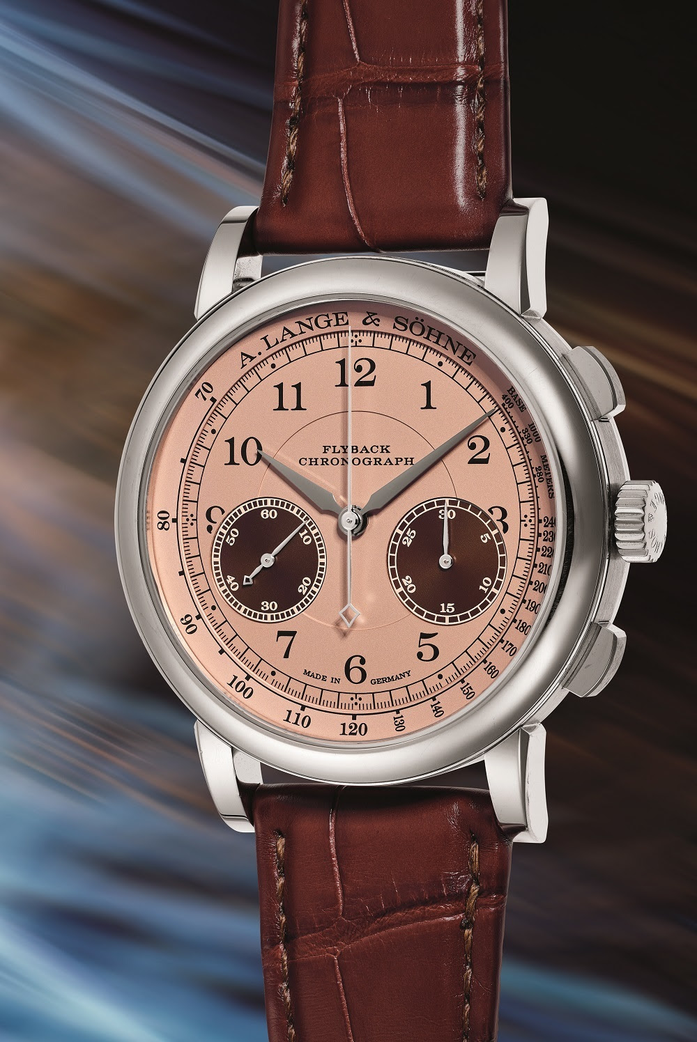 Un lussuoso orologio da polso con cinturino in pelle marrone, quadrante in oro rosa, numeri neri, due quadranti secondari e cassa in acciaio lucido, che evoca l'eleganza di Rolex o Patek, su uno sfondo astratto sfumato. Il quadrante riporta la scritta "A. Lange & Söhne Flyback Chronograph".