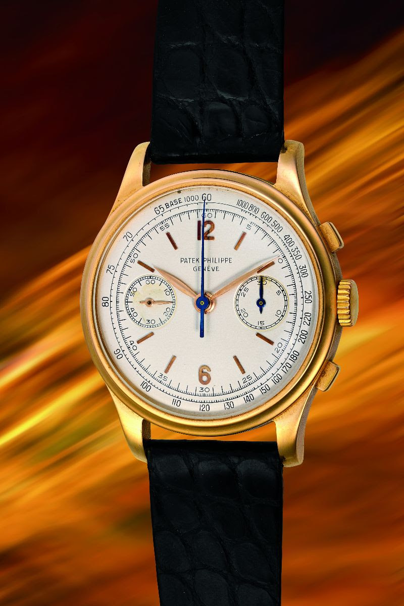 Un orologio da polso Patek Philippe in oro con quadrante bianco, lancette blu e cinturino in pelle nera è esposto su uno sfondo sfumato e striato di arancione e giallo, evocando l'eleganza di un Rolex in un'asta esclusiva.