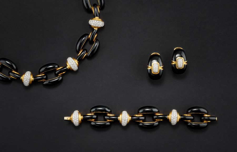 Un set di gioielli coordinati composto da collana, bracciale e orecchini con maglie nere, dettagli in oro, perle naturali asta e sezioni tempestate di piccoli diamanti, il tutto su uno sfondo nero.