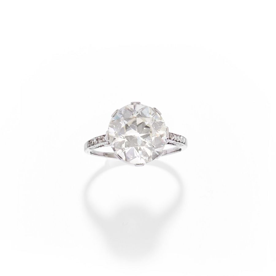 Un anello in oro bianco o platino con un grande diamante solitario rotondo, perle naturali e diamanti più piccoli incastonati lungo la fascia, il tutto su uno sfondo bianco.