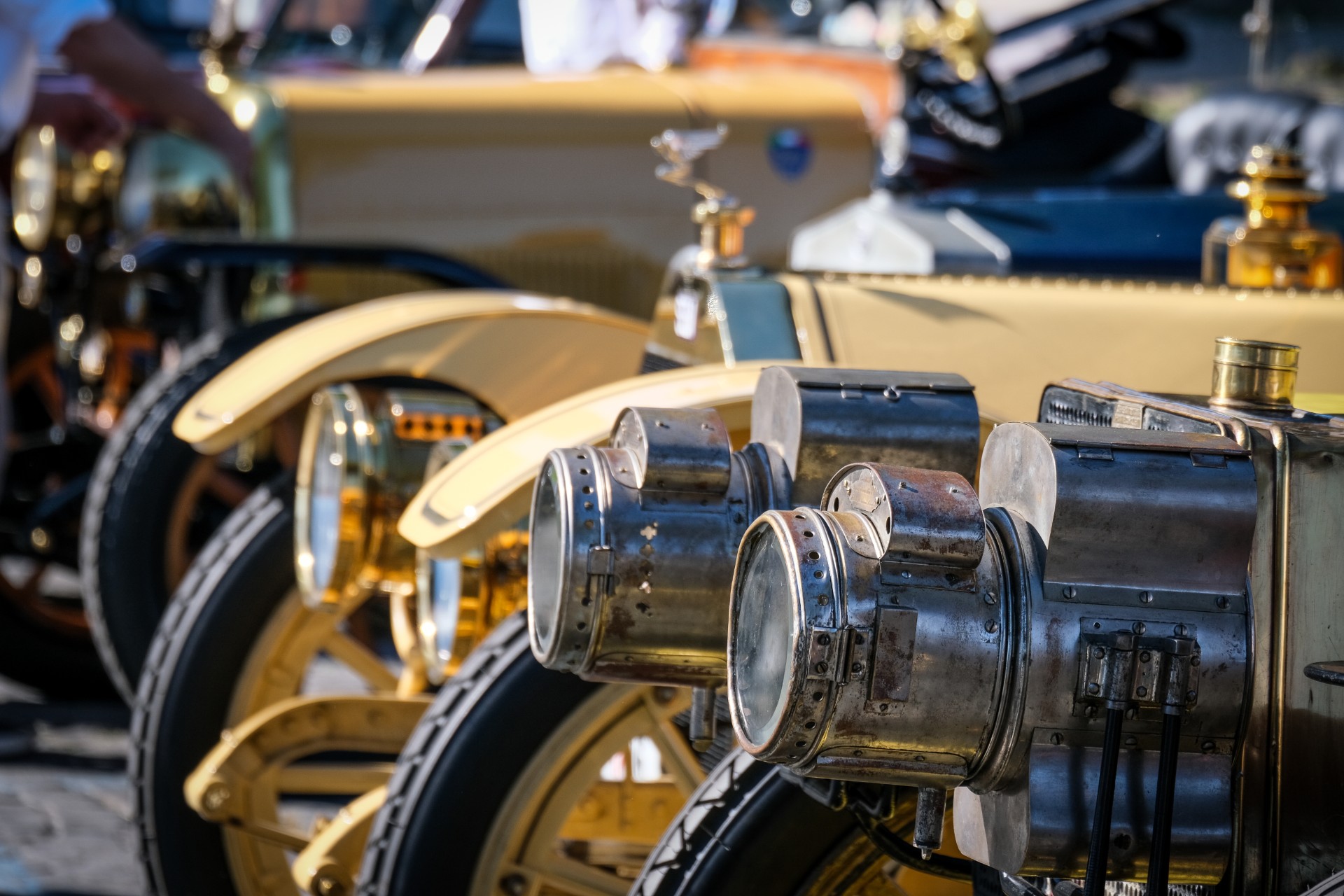 Vista ravvicinata dei fari e dei dettagli anteriori di diverse auto gialle d'epoca allineate a un evento di auto storiche giubileo, con parti metalliche lucide e disegni intricati che catturano la luce del sole.