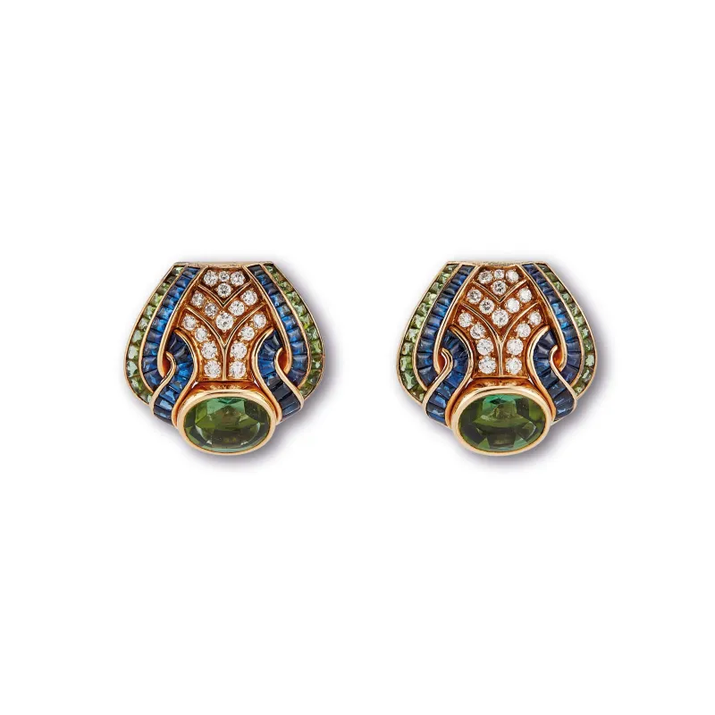 Un paio di orecchini decorati con dettagli in oro, blu e verde, pavé di diamanti e una prominente pietra verde ovale al centro. Questo design di ispirazione art déco trasuda un lusso che ricorda un capolavoro Patek Philippe Nautilus.