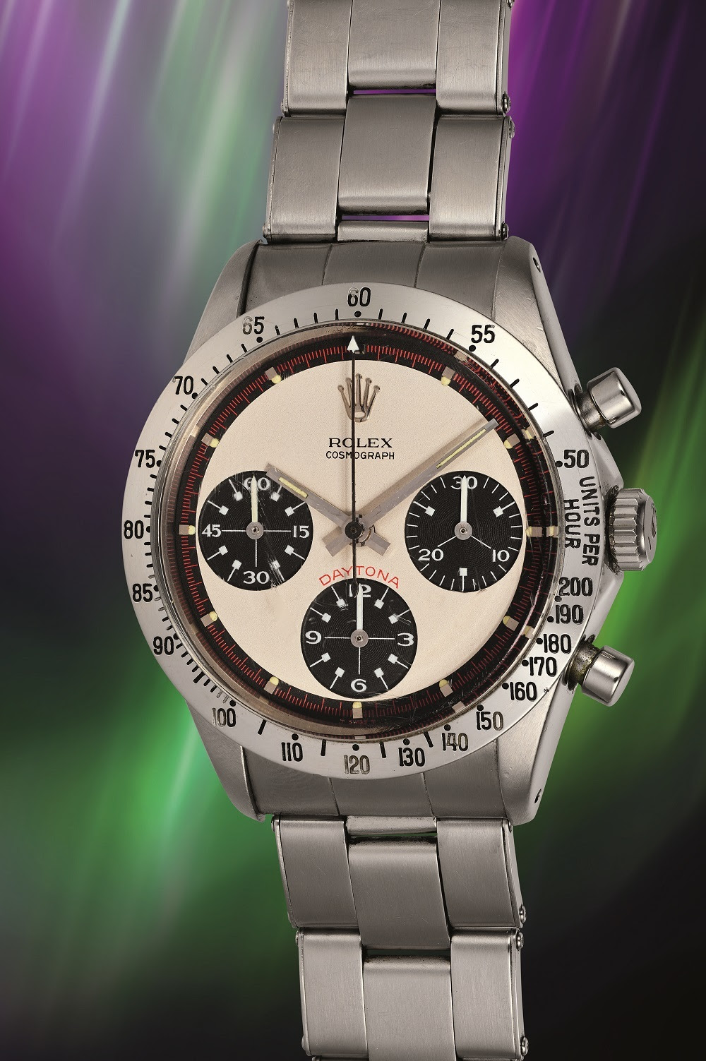 Un orologio Rolex Cosmograph Daytona d'epoca con quadrante argento e nero, tre quadranti secondari e bracciale in acciaio inossidabile, esposto su uno sfondo viola e verde vivace, che ricorda l'aurora: perfetto per ogni appassionato di Rolex Patek Asta.