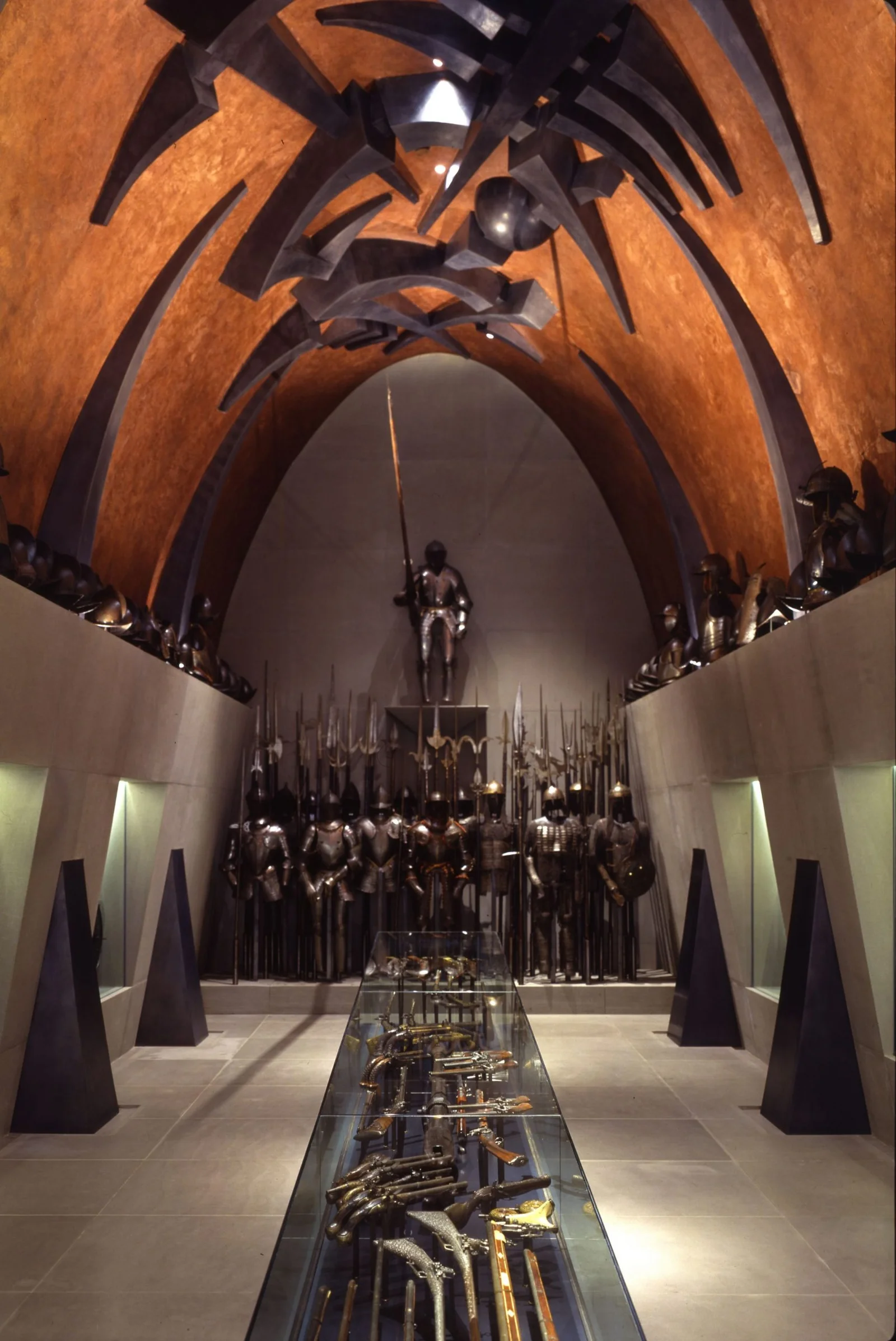 In una sala dal soffitto arancione ad arco sono esposte armature e armi medievali. In mezzo a teche di vetro con spade e pistole si trova una statua di cavaliere, la cui posa ricorda le sculture di Arnaldo Pomodoro, mentre armature e armi da fuoco sono allineate alla parete di fondo.