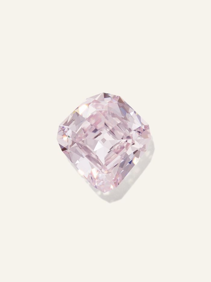 Un diamante rosa chiaro taglio cuscino con superfici sfaccettate riflette la luce, messa in risalto da uno sfondo semplice, bianco sporco.
