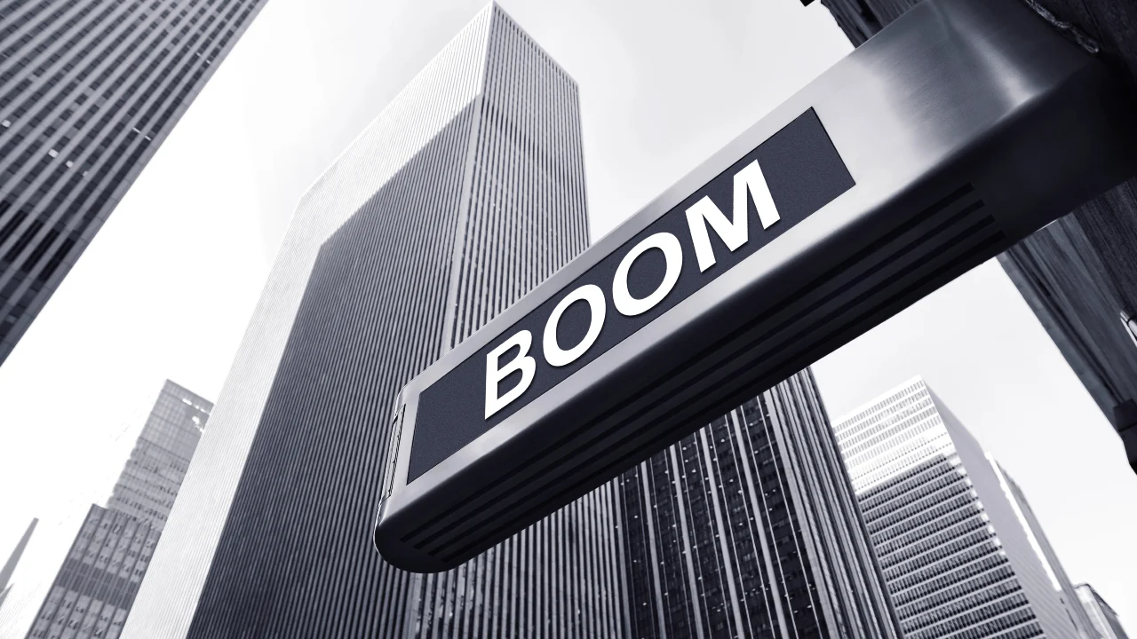 Una grande insegna con la parola "Boom” a caratteri cubitali si staglia su alti e moderni grattacieli, catturando il polso delle tendenze del mercato immobiliare. La combinazione di colori bianco e nero mette in risalto il dinamico paesaggio urbano.