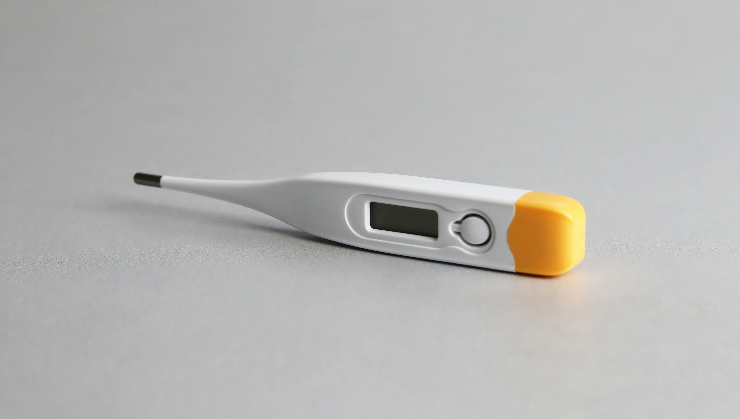 Un termometro digitale con corpo bianco, cappuccio giallo e piccolo display si trova su una superficie grigio chiaro.