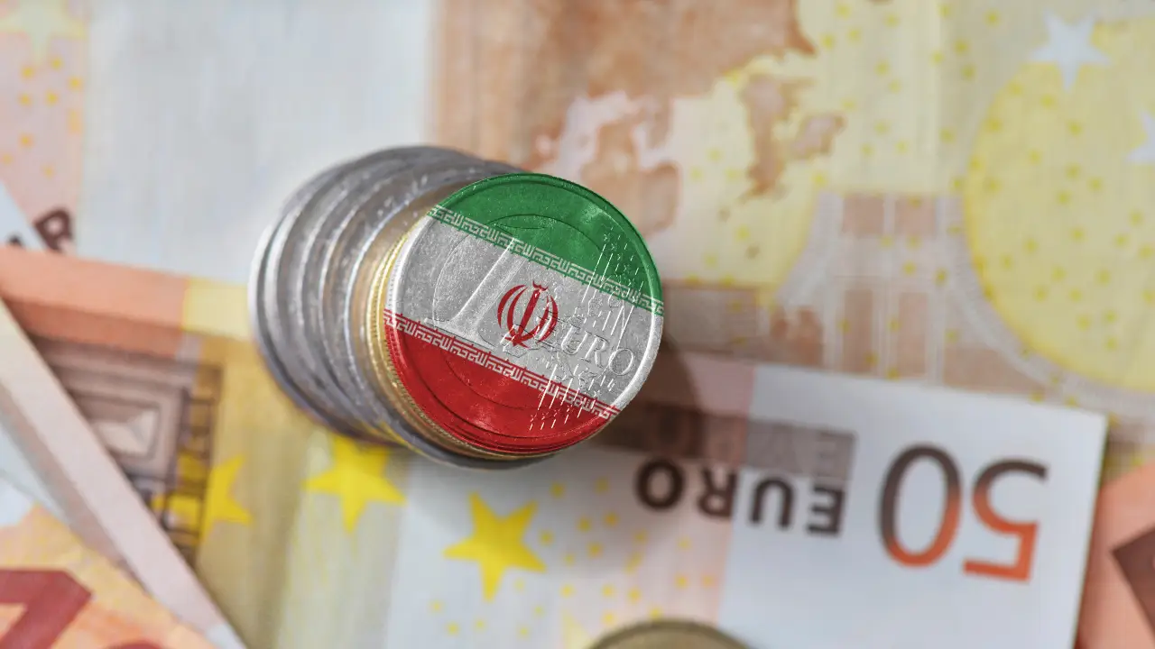 Una pila di monete dipinte con la bandiera iraniana in cima poggia su varie banconote in euro, tra cui una banconota da 50 euro visibile.