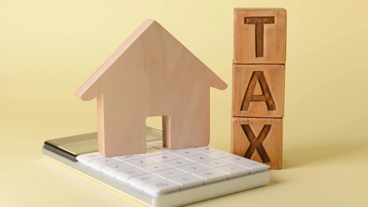 Un modello di casa in legno e blocchi di legno con la scritta "Tax" si trovano in cima a una calcolatrice, a simboleggiare l'impatto della tassazione sui fondi immobiliari e più imparticolare sul fondo estero.