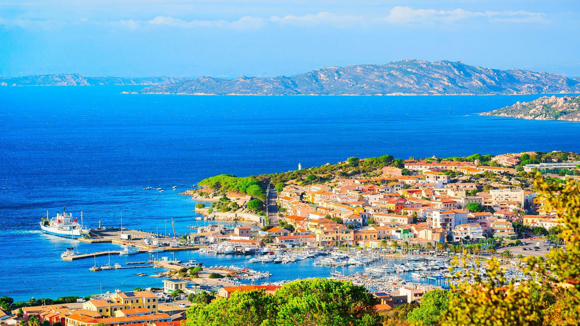 Una vivace cittadina costiera con edifici colorati, un vivace porto turistico pieno di barche, un mare limpido e azzurro e lontane colline rocciose sotto un cielo soleggiato: una vera esperienza di casa lusso mare.