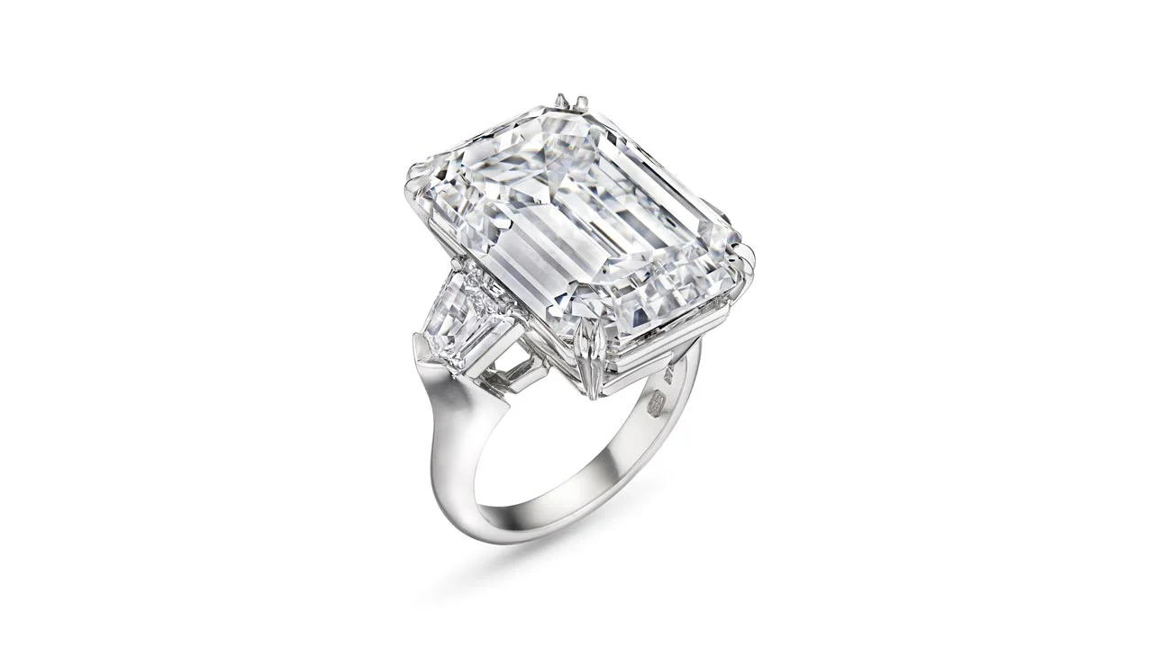 Anello in platino con un grande diamante rettangolare dal taglio smeraldo e diamanti laterali a baguette che ricordano i pezzi dell'asta record di Maria Antonietta, incastonati su uno sfondo bianco.