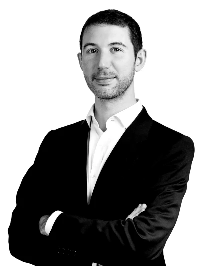 Un uomo in giacca e cravatta con camicia bianca sta in piedi con le braccia incrociate e guarda con sicurezza verso l'obiettivo su uno sfondo bianco, catturando lo spirito professionale che spesso si vede nella dinamica scena imprenditoriale di Dubai.