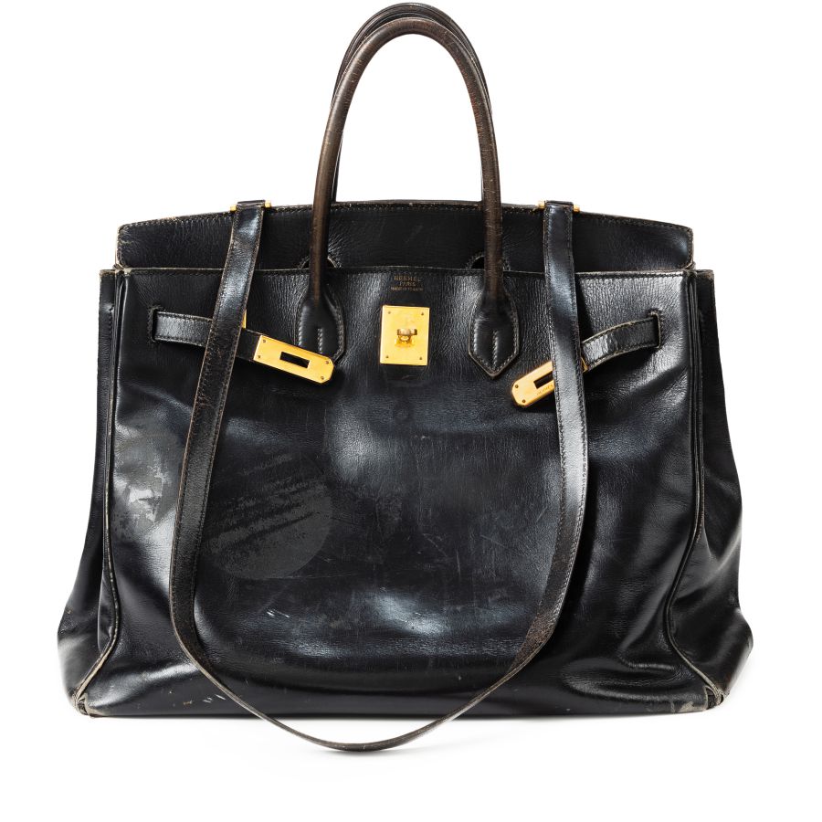 Una borsa Jane Birkin in pelle nera usurata con finiture dorate, due manici e graffi e segni visibili sulla superficie.