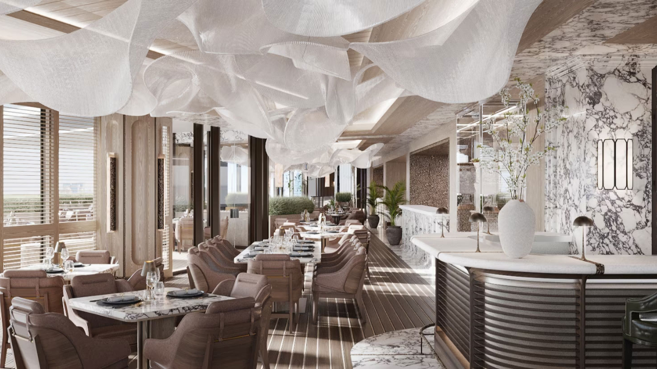 Un ristorante moderno ed elegante a Dubai, con accenti in marmo, mobili in legno e decorazioni in tessuto bianco che pendono dal soffitto, crea un'atmosfera ariosa ed elegante. I tavoli sono apparecchiati per mangiare e le grandi finestre lasciano entrare la luce naturale.