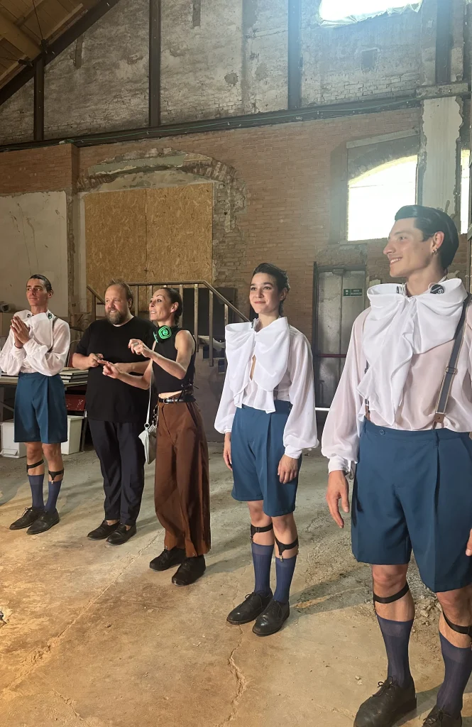 Cinque persone in piedi all'interno di uno spazio rustico, alcune vestite allo stesso modo, sembrano applaudire o festeggiare, forse ispirate dallo spirito giocoso di Maurizio Cattelan Santa.