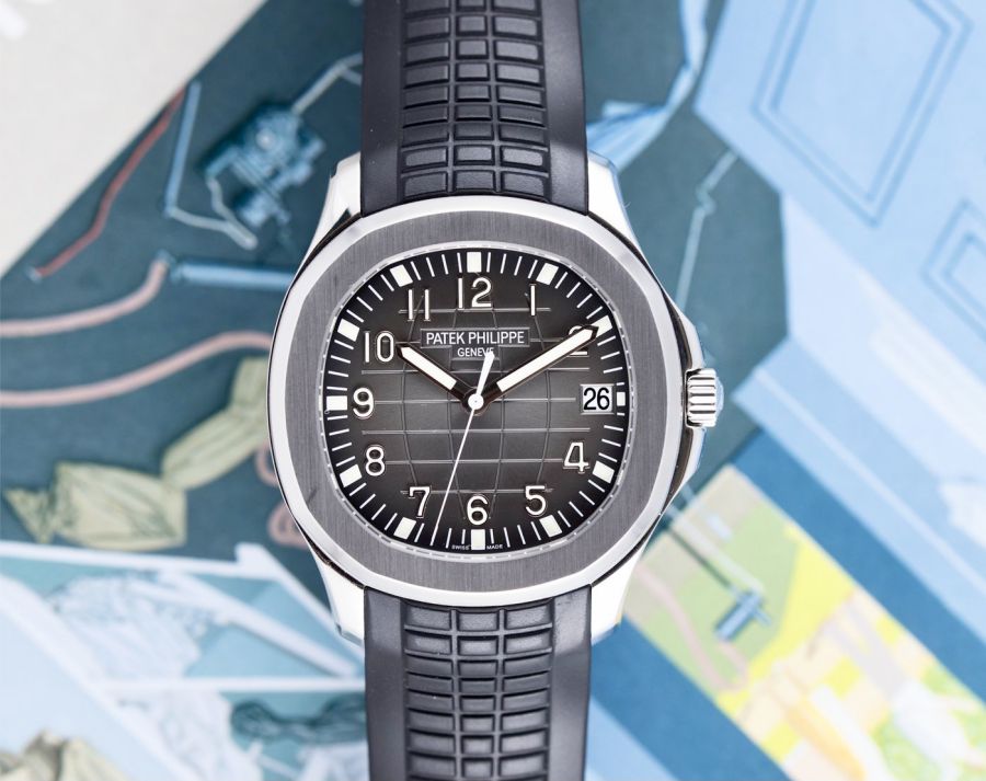 Un orologio da polso Patek Philippe Aquanaut con quadrante nero testurizzato, numeri bianchi e cinturino in caucciù nero abbinato è esposto su uno sfondo illustrato e colorato: una scelta ideale per un orologio. La data è fissata al 26.