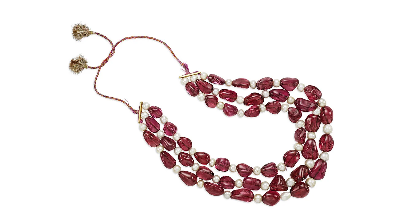 Una collana a tre fili con pietre rosse di forma irregolare e perle bianche rotonde, infilate in un cordoncino rosso con accenti dorati e lacci con nappe: un design che ricorda l'eleganza record di Maria Antonietta.