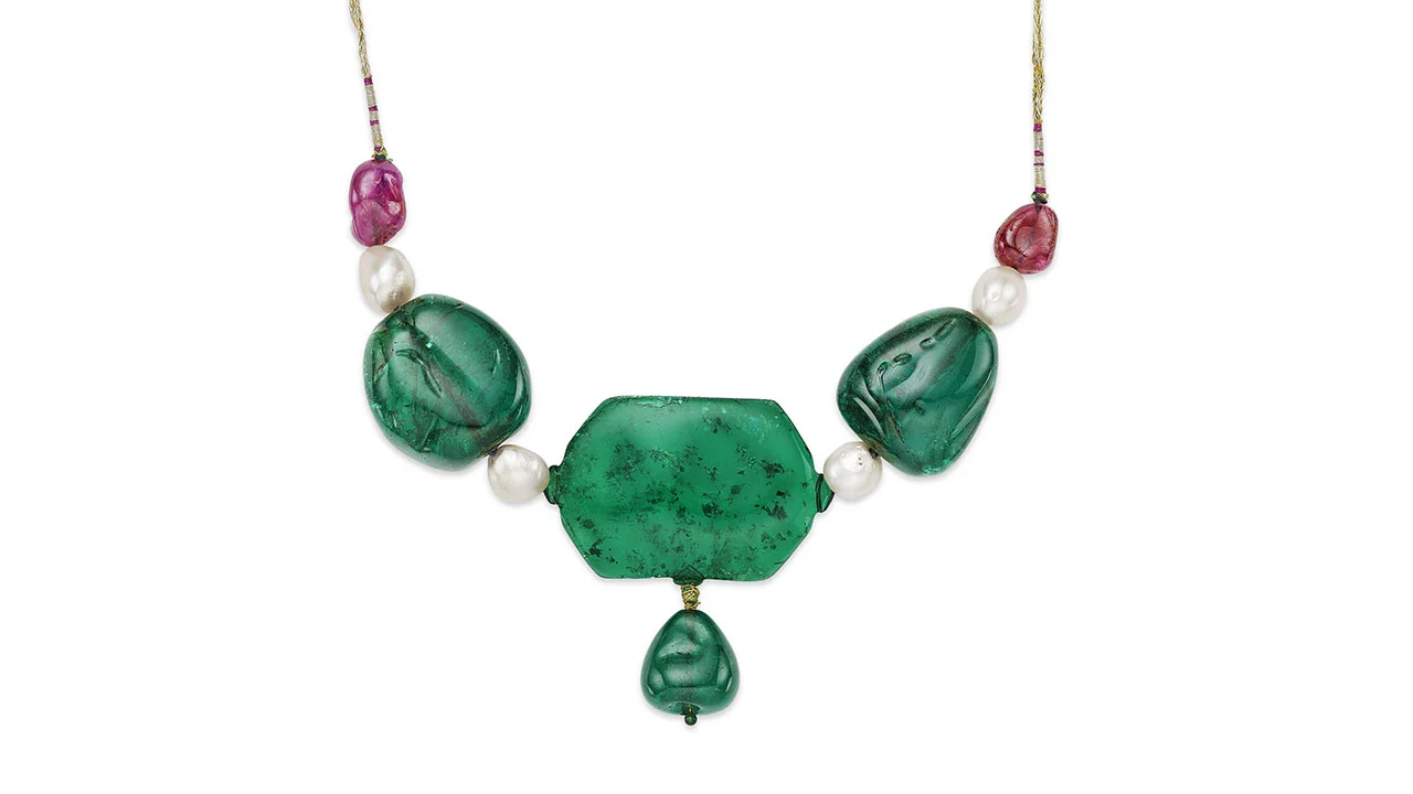 Una collana ispirata a Maria Antonietta, con tre grandi pietre verdi - una centrale e due laterali - accentuate da perle bianche e perline rosa, il tutto infilato in una sottile catena d'oro che ricorda un'asta da disco.